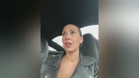 Media: Video of a woman in a black leather jacket, driving a car, with a blurred background.