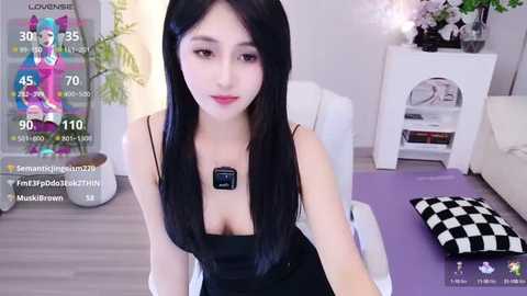 Media: A video of an Asian woman with long black hair and fair skin, wearing a black dress, seated in a modern living room.