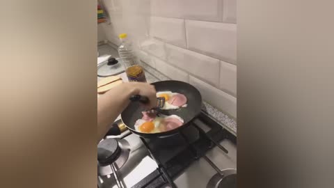 Media: Video of a person cooking scrambled eggs on a stovetop in a kitchen with white tiled walls. The person's hand is holding a spatula over the pan.