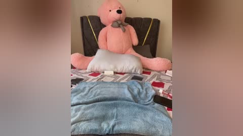 Media: Video of a pink plush teddy bear on a bed with a gray patterned duvet and a blue towel, a remote control on the floor.