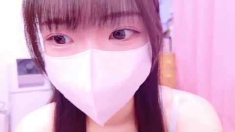 Media: Video of an East Asian woman with long, straight black hair, wearing a white face mask, white tank top, and pink background.