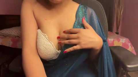 Media: Video of a woman with medium skin tone, wearing a blue satin robe, exposing a white lace bra revealing her breasts, with red manicured hands covering one breast.