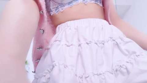 Media: Video of a pale-skinned woman in a delicate, light-pink satin robe with lace trim, revealing a lacy white bra and a voluminous, layered white skirt.