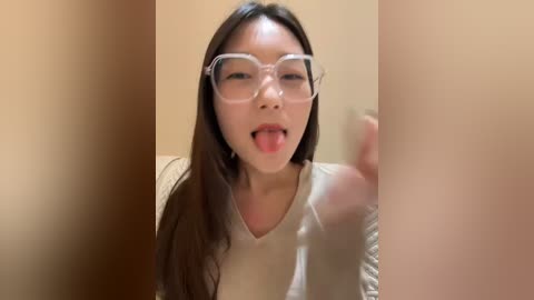 Media: Video of an Asian woman with long, dark hair, wearing clear-framed glasses and a white top, sticking her tongue out playfully.