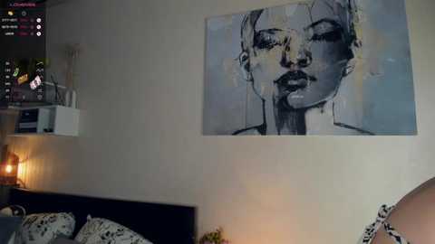 Media: Video of a minimalist bedroom with a large, abstract black-and-white painting of a woman's face on the wall. A modern bed with white pillows and a black headboard is visible.