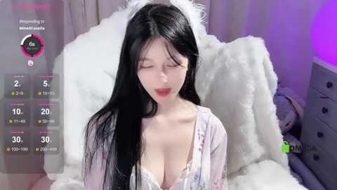 Media: Video of an East Asian woman with long black hair, wearing a revealing white lingerie top, lying on a white fluffy bed. The room has a purple light.