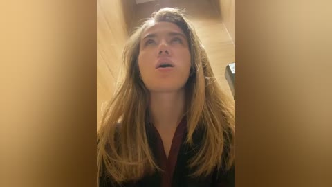 Media: A video of a young woman with long, light brown hair, fair skin, and a maroon robe, looking upward with a slightly open mouth, set against a blurred, warm-toned background.