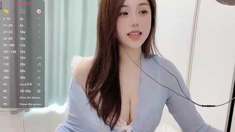 Media: Video of an East Asian woman with long brown hair, fair skin, and light blue cardigan, sitting in a modern room with a medical device and soft lighting.