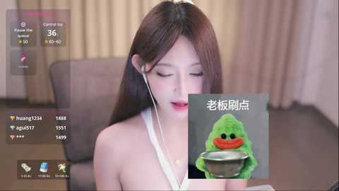 Media: A video of an Asian woman with long brown hair, wearing a white tank top, sitting in a living room. She's listening to music on white earbuds. A green plushie duck is in the foreground.