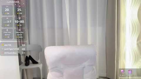 Media: A video of a minimalist room featuring a white chair, white curtains, a white table, and a pair of black high heels on the table. A digital interface with a clock and temperature display overlays the scene.