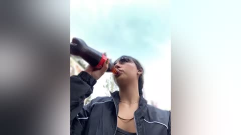 Media: A video of a young woman with short dark hair, wearing a black jacket and red lipstick, drinking from a black water bottle.