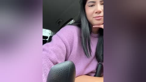 Media: A video of a woman with long black hair, wearing a purple sweater, sitting in a chair with headphones on, possibly recording.