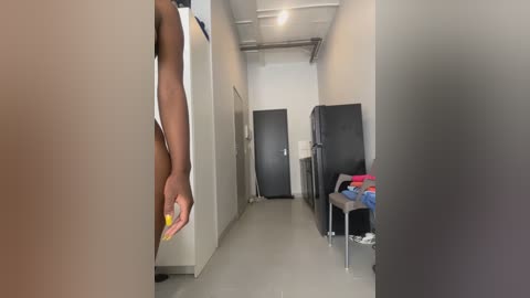 Media: Video of a narrow, dimly lit hallway with beige walls, a black fridge, and a person's arm with yellow fingernails reaching through a door.