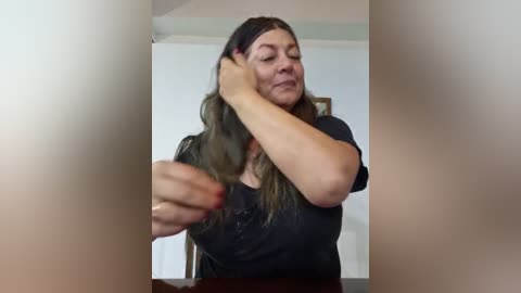 Media: Video of a middle-aged woman with long, wavy brown hair, wearing a black t-shirt, adjusting her hair in a mirror.