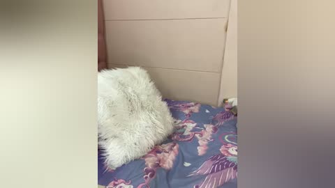 Media: Video of a cozy bedroom corner with a fluffy white pillow on a bed covered in a colorful floral duvet. The walls are light beige, and the room exudes a warm, inviting atmosphere.