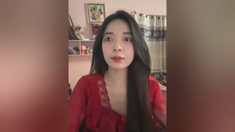 Media: Video of a young Asian woman with long black hair, wearing a red top, in a cozy, cluttered bedroom with framed art, shelves, and a curtain.