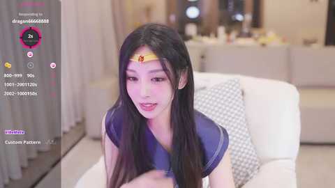 Media: A video of a young Asian woman in a blue sailor uniform with a yellow headband, posing on a white couch. Background shows a modern, warmly-lit living room.