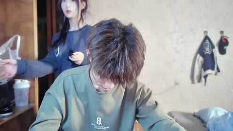 Media: Video of a young man with messy hair receiving a haircut in a salon. The stylist, with long black hair, wears a dark top.