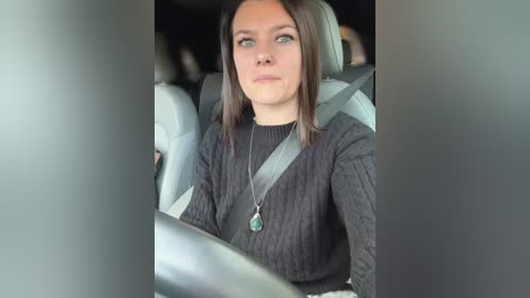 Media: A video of a young woman with shoulder-length brown hair, wearing a black knit sweater, and a silver seatbelt, driving in a car.