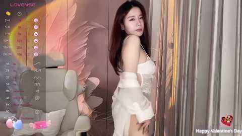 Media: Video of a young Asian woman with long, dark hair, wearing a white, lace lingerie set, standing in a modern, minimalist room with a large mirror and white chair.