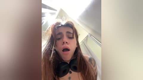 Media: Video of a young woman with long brown hair, wearing black headphones, and lying on a bed with a ceiling fan visible, looking relaxed and content.