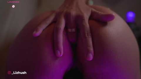 Media: Video of a hand with manicured nails and a ring, spreading a person's buttocks, revealing genitals. The background is blurred, with purple lighting.