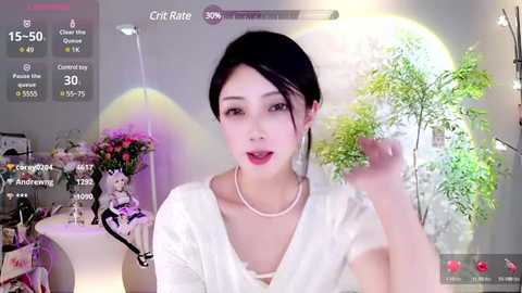 Media: A video of an East Asian woman with black hair in a bun, wearing a white top and pearl necklace, holding a green leaf in a virtual livestream, with a background featuring a large, glowing moon.