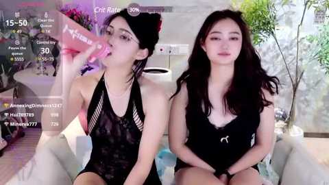 Media: Video of two Asian women in black lingerie, one drinking from a pink dildo, the other sitting seductively. Background features a modern room with a potted plant.