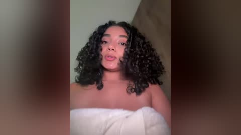 Media: Video of a young Black woman with curly hair wrapped in a white towel, partially obscured by a blurred object in the foreground.