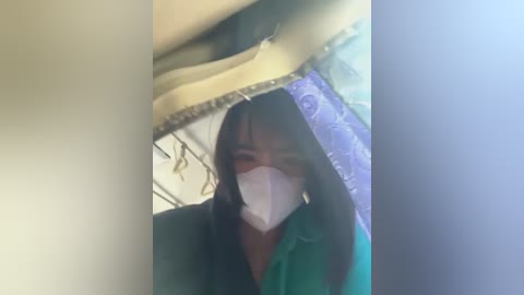 Media: A video shows a woman with medium skin tone, long dark hair, and a white mask, standing under a yellow umbrella with a blue floral pattern. She wears a green jacket.