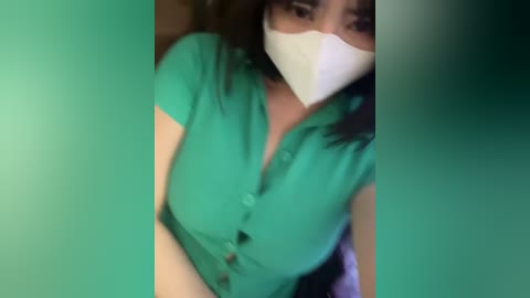 Media: A blurry video shows a woman with long dark hair, wearing a green blouse, white mask, and a white bandana.