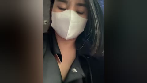 Media: A close-up video of a person wearing a white face mask, black shirt, and black blazer, with eyes closed, likely sleeping.