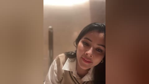 Media: Video of a young Asian woman with long black hair, wearing a white shirt and beige vest, peering through a bathroom door, creating a voyeuristic, intimate atmosphere.