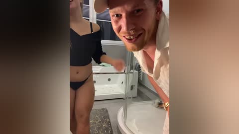 Media: A video showing a woman in a black crop top and underwear, and a man in a white shirt, leaning over a bathtub in a bathroom.