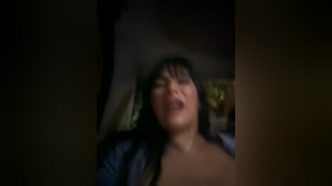 Media: A dimly lit video captures a woman with long black hair, closed eyes, and an open mouth, suggesting ecstasy. She is wearing a blue shirt, lying on a bed with a pillow, in a bedroom setting.