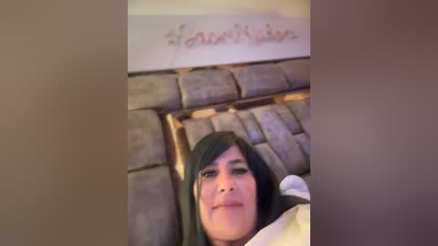 Media: A blurry video of a person with dark hair, possibly Middle Eastern, lying on a gray, cushioned bench. The background shows a white wall with red graffiti.