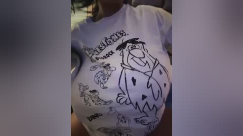 Media: Video of a pregnant woman wearing a white \"Pee Wee's Playhouse\" t-shirt, featuring cartoon characters, in a dimly lit room.