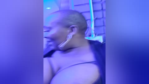 Media: A video shows a bald, light-skinned man wearing white earbuds and a black tank top, standing in a dimly lit room with blue ambient lighting and brick walls.