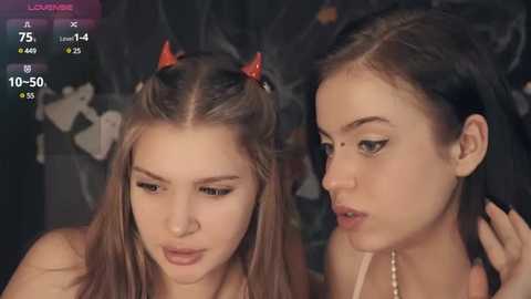 Media: Video of two young women, one with devil horns, the other with a pearl necklace, both with pale skin, in a dimly lit room, displaying a virtual reality interface.