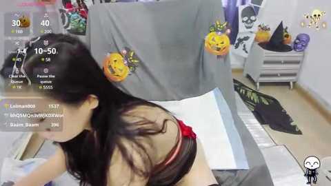 Media: A video of a woman with long black hair, wearing a black bra, sitting at a desk with Halloween decorations in the background.