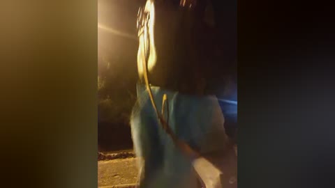 Media: A dimly-lit video of a person in a blue hoodie, carrying a large black backpack, walking on a sidewalk at night, with blurred background lights.