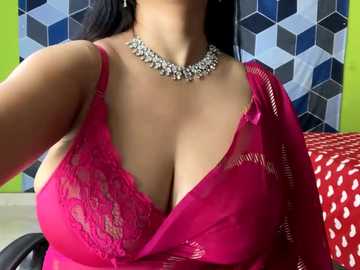 Media: Video of a woman in a vibrant pink lace bra, showcasing ample cleavage, with a statement choker and green wall in the background.