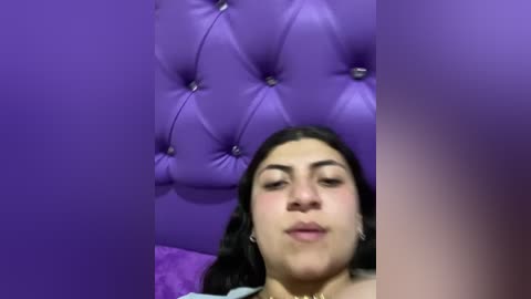 Media: A video of a young woman with medium skin tone, dark hair, and full lips, against a purple, tufted leather headboard. She wears a light-colored top.