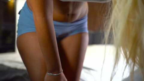 Media: A video of a blonde woman in light blue shorts, leaning forward, showing her toned midriff and slender legs, with a blurred background.