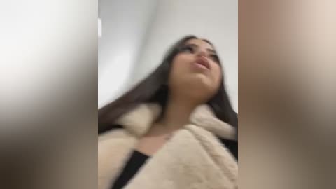 Media: A blurred video of a woman with long, dark hair, wearing a beige, fluffy robe, seen from below, with her head tilted back.