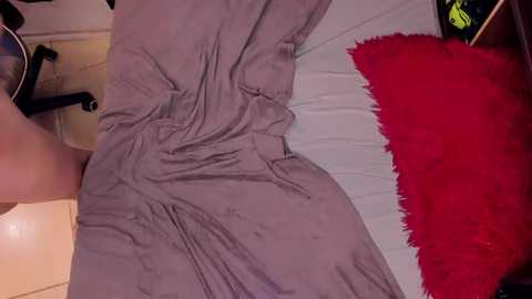 Media: Video of a person lying on a bed with a gray sheet and a red fuzzy rug, visible from the waist up.