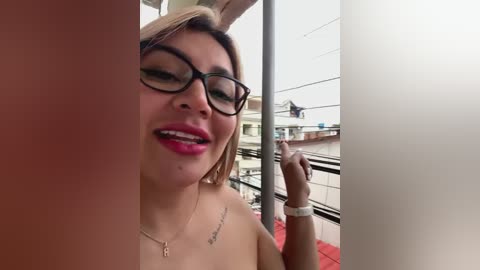 Media: Video of a smiling, fair-skinned, curvy woman with glasses, pink lipstick, and a tattoo, holding a cigarette on a balcony.