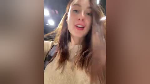 Media: A video of a young Caucasian woman with straight, shoulder-length brown hair, fair skin, and a slender build, wearing a beige sweater. She has a relaxed expression with slightly parted lips.