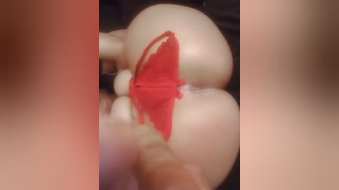 Media: A close-up video of a person's buttocks, with a red lace thong partially pulled down, revealing a portion of the anus. The background is blurred and dark, making the red fabric stand out prominently.