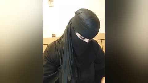 Media: A video of a person wearing a black niqab and matching robe, with their face hidden, standing in a dimly lit hallway.